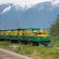 A train travels through a forest against the backdrop of a snowy mountain